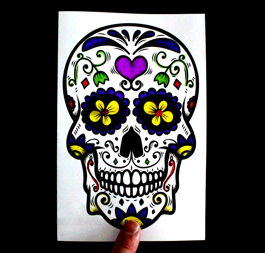Colored-in sugar skull image with red LEDs in the center of each eye and a finger pressing down on a switch to close the circuit and make the eyes/LEDs glow.